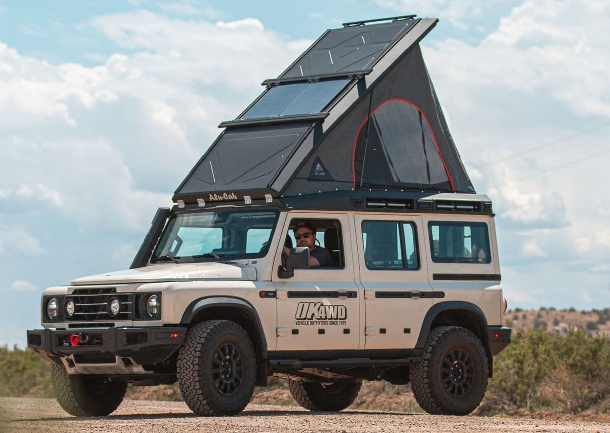 Beige SUV with a Alu-Cab Silenus Roof Conversion  on a dirt road under a blue sky