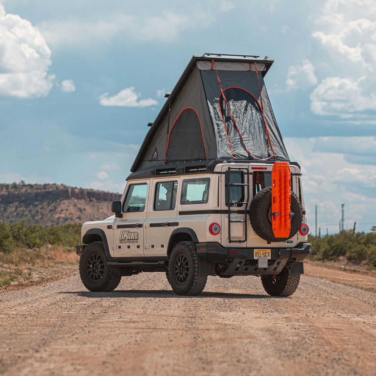Beige INEOS Greandier SUV with a ALU-CAB Silensu Roof conversion on a dirt road with a scenic background