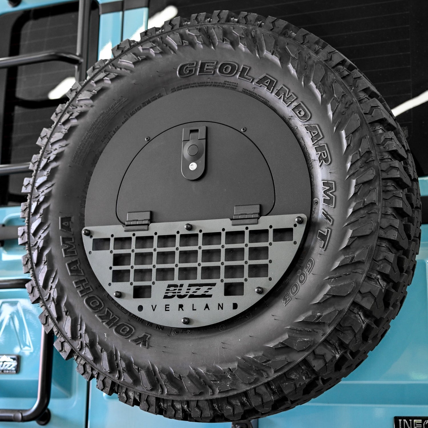 Buzz Overland Spare Wheel Storage Cubby mounted on INEOS Grenadier 17-inch wheel, showcasing durable 5052 aluminium construction and textured black powder coat finish for overlanding adventures