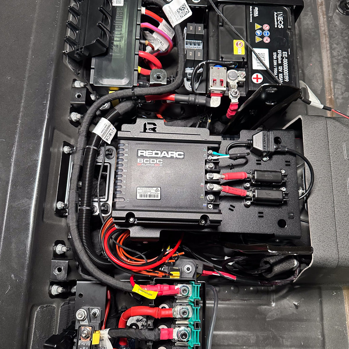 Alpha50 R charger mount under the INEOS Grenadier rear seat, between starter and auxiliary battery
