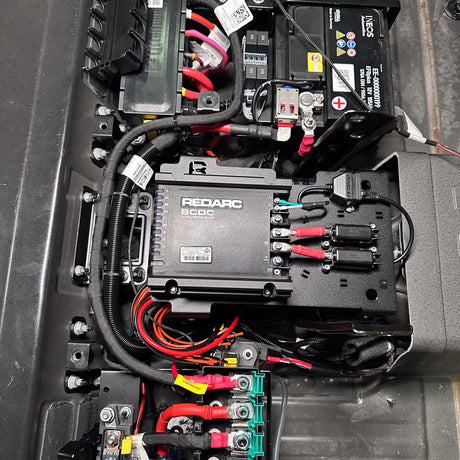 Alpha50 R charger mount under the INEOS Grenadier rear seat, between starter and auxiliary battery